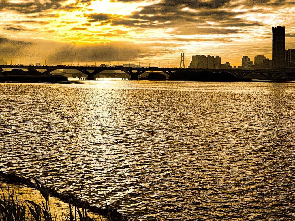 傍晚时分，夕阳缓缓自桥边落下，淡水河面洒染着金黄色彩